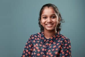 A smiling young woman in a blue floral shirt against a grey background, seen in our pediatric dental FAQs.