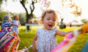 A young child laughing while playing with colorful ribbons outdoors, pictured near a display of pediatric dental FAQs.