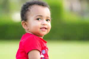 A toddler in a red shirt looking over their shoulder at the camera, featured in our pediatric dental FAQs.