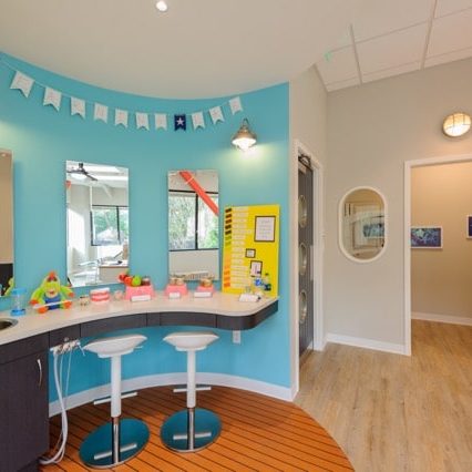 A pediatric dental office with two stools at a curved counter, mirrors, and a bright blue wall decorated with bunting.
