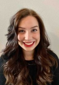 A smiling woman with long, dark hair wearing a black top.