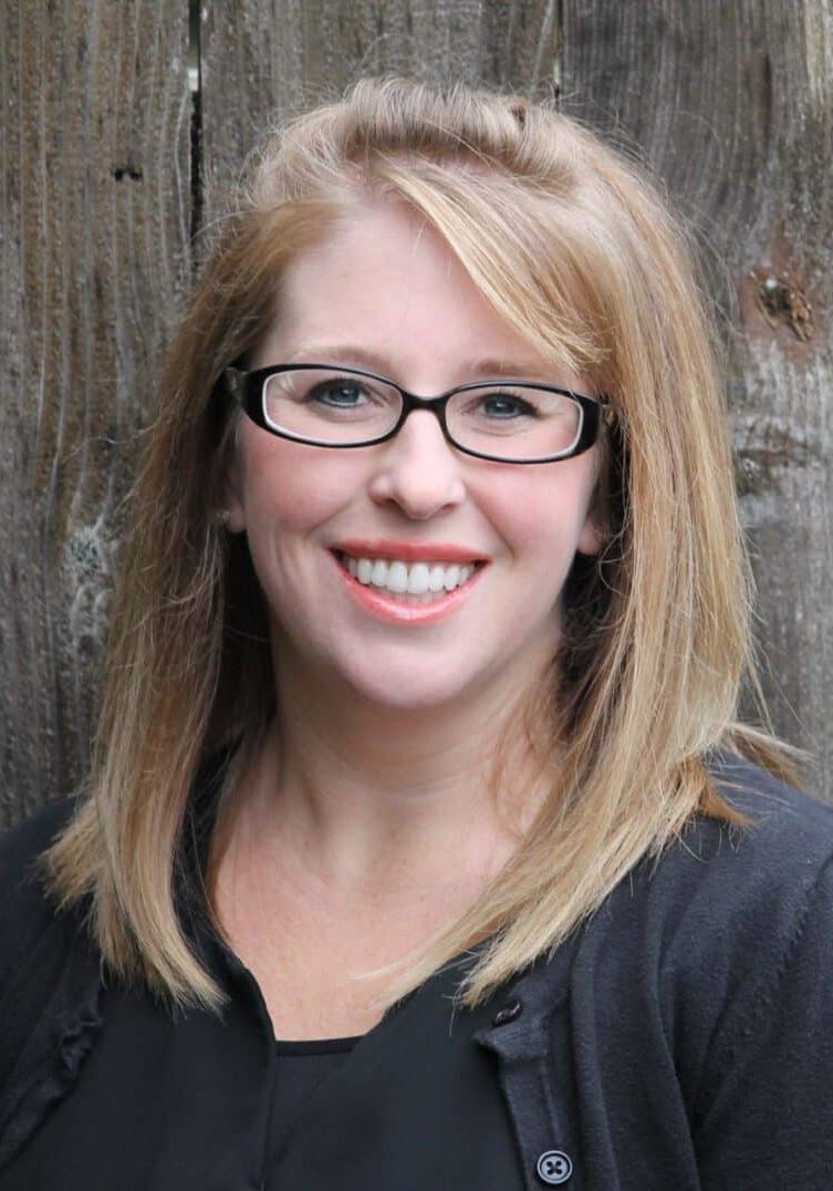 A smiling woman with shoulder-length blonde hair and black-framed glasses.