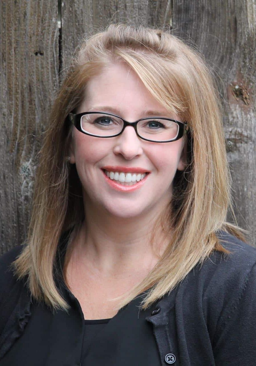 A smiling woman with shoulder-length blonde hair and black-framed glasses.