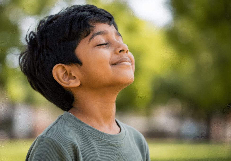 A young boy with his eyes closed and head tilted back outdoors, representative of pediatric airway dentistry in Mill Creek.